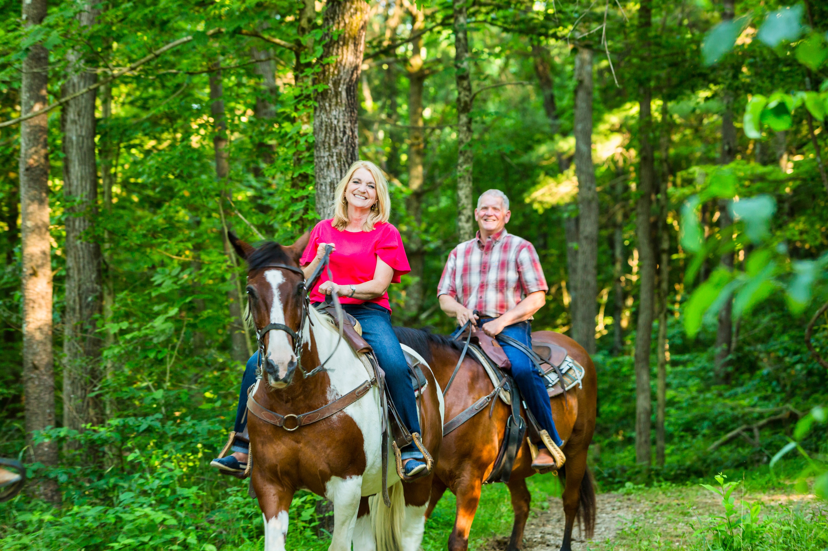 a man and woman riding horses in the woods
