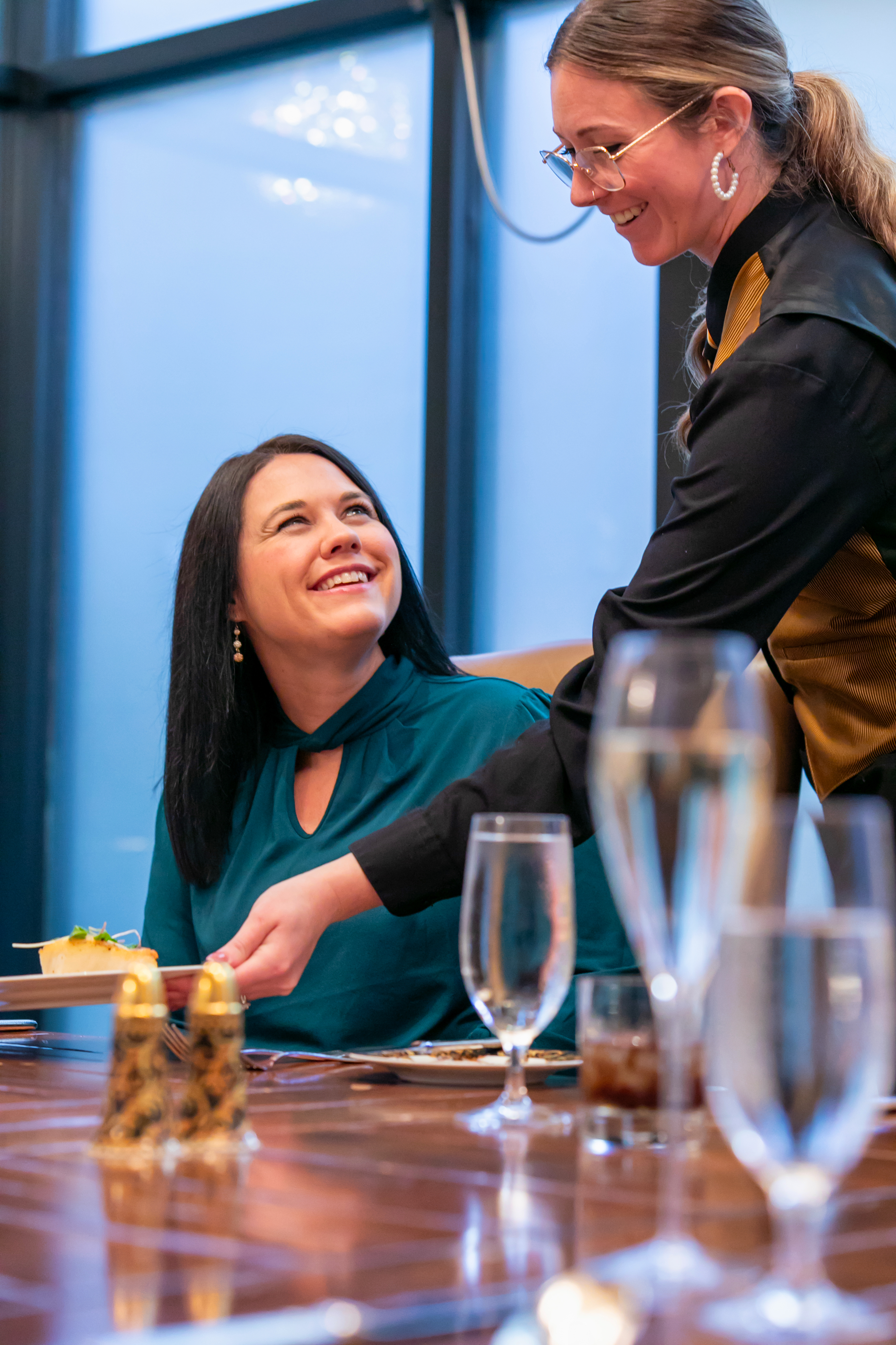 a woman smiling at a table with a waiter