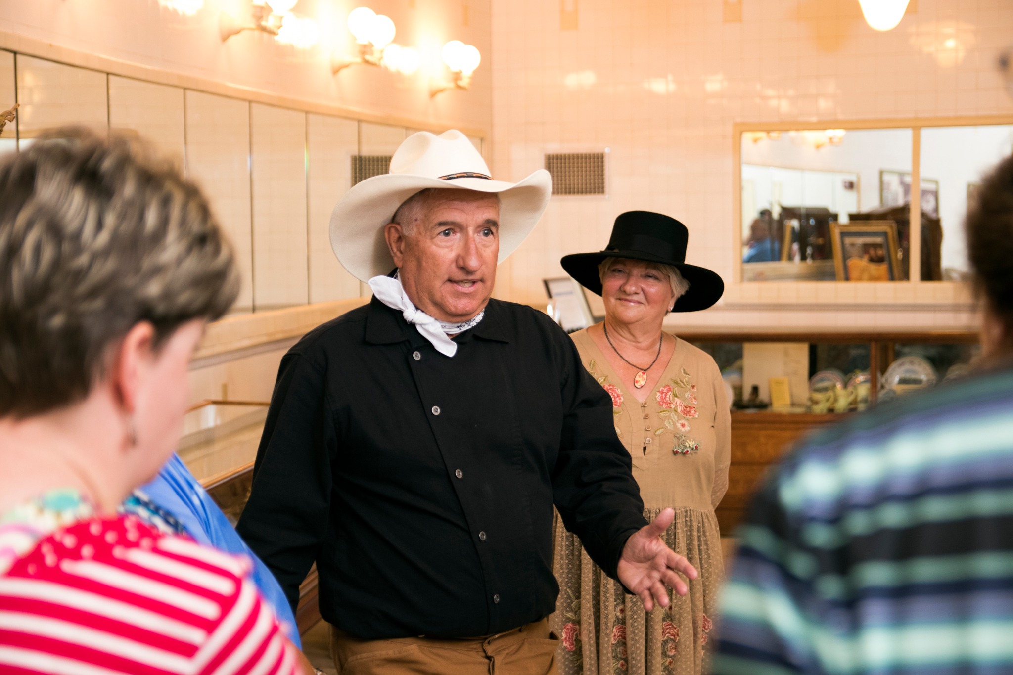 a man in a cowboy hat and black shirt talking to a group of people