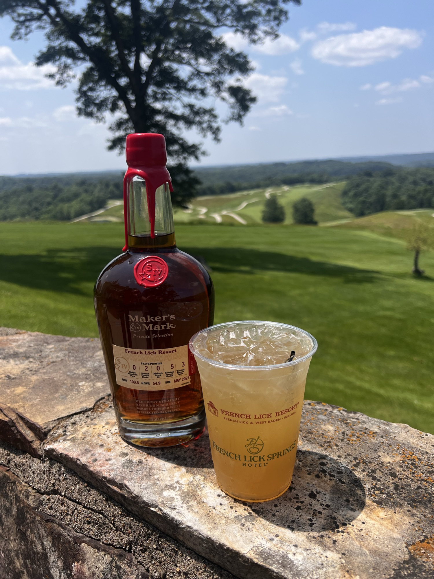 a bottle of alcohol and a cup of liquid on a stone ledge
