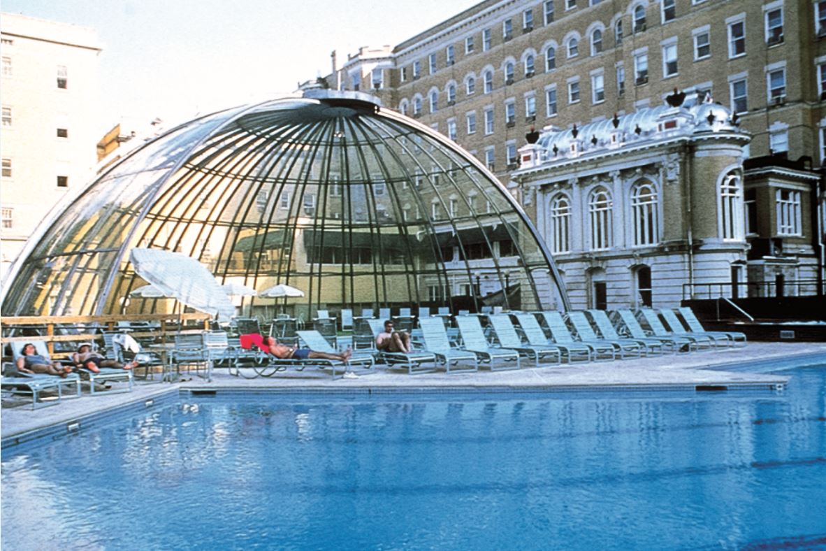 a pool with a dome roof and people sitting in lounge chairs