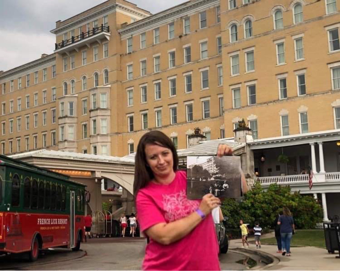 A woman holding a photo in front of a hotel