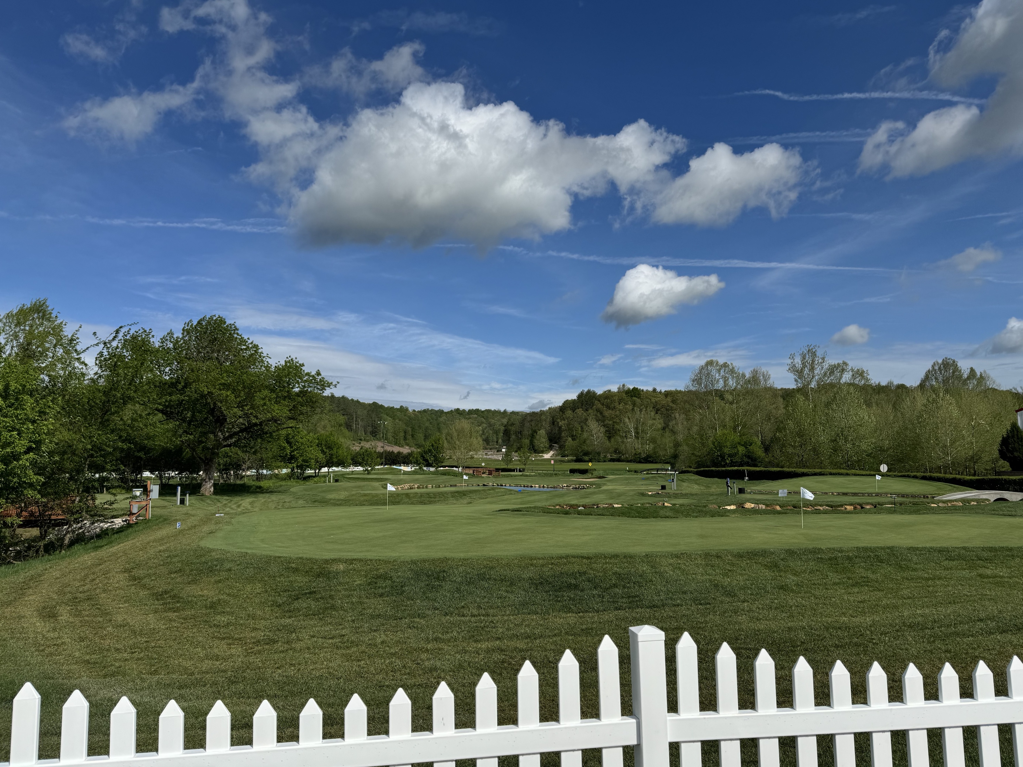 a white picket fence and a field with trees and blue sky