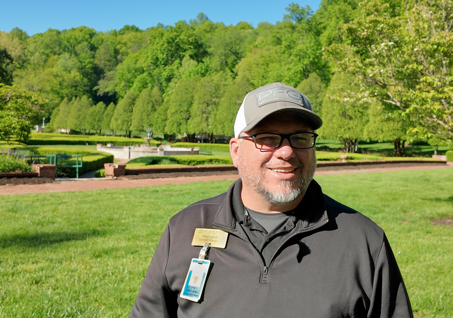 a man in a hat and glasses standing in a park