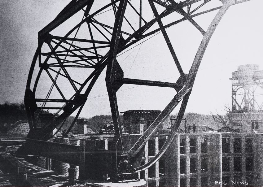 a large metal structure with a building behind it