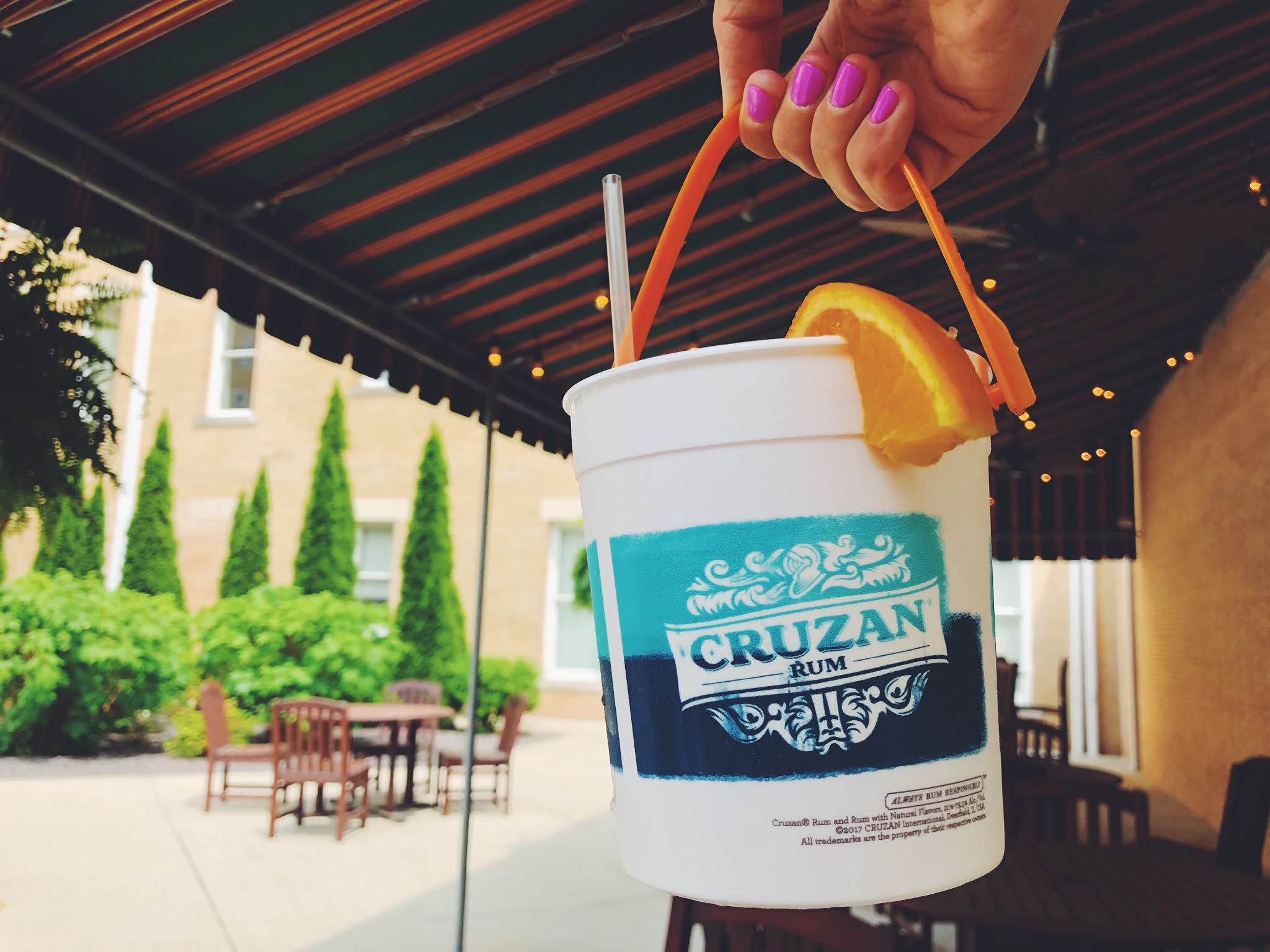 a hand holding a white bucket with a straw and orange slice